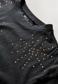 Zwarte T-shirt van zacht stof met een verspreid patroon van roségouden studs aan de voorkant. Ronde halslijn, korte mouwen, casual pasvorm.