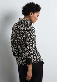 Czarnobiała bluzka w wzory z wysokim kołnierzem, długimi rękawami i czarnymi mankietami, z geometrycznym wzorem liści na miękkim materiale.