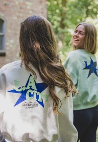 Witte sweatshirt met "L.A. CITY" in groen en blauw en een sterontwerp; een tweede lichtgroene sweatshirt zichtbaar op de achtergrond.
