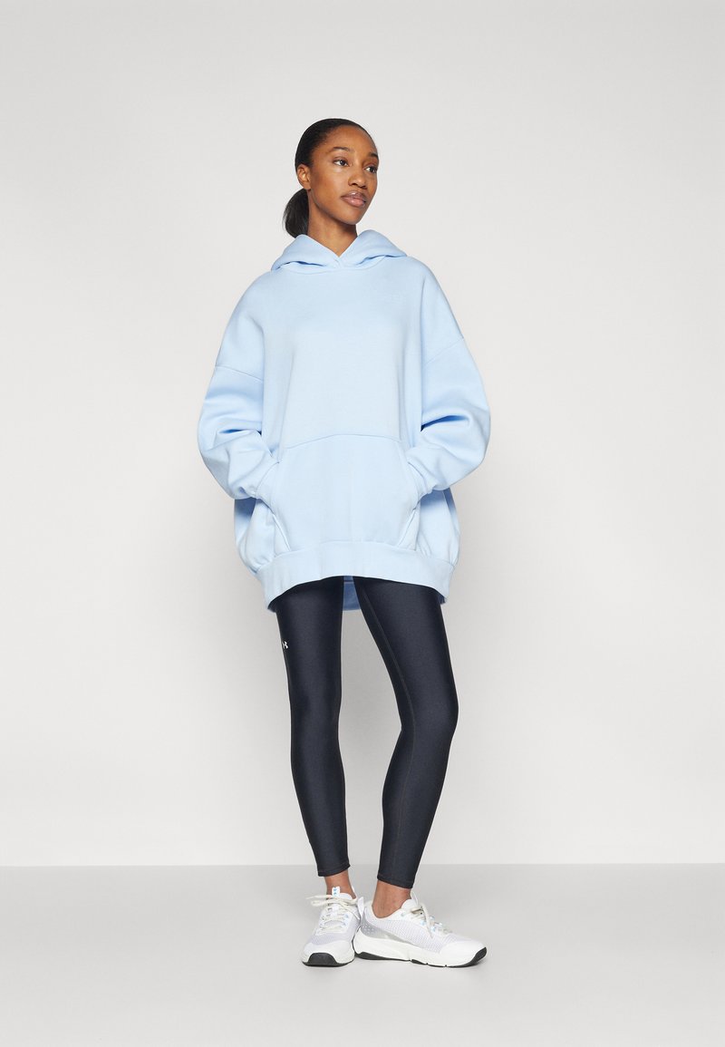 Helles blaues, übergroßes Hoodie mit einer Kängurutasche, kombiniert mit dunklen Leggings und weißen Sneakers. Verfügt über eine lockere Passform und eine Kapuze mit Kordelzug.