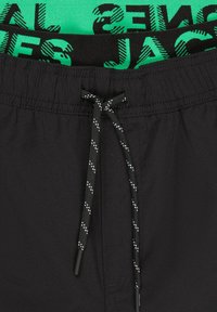 Bañador negro con una cintura elástica negra y verde que incluye un logo, cordón ajustable y textura suave.