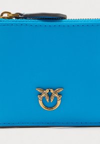 Λαμπερό μπλε δερμάτινο τσαντάκι με χρυσό έμβλημα δύο πουλιών και κλείσιμο με φερμουάρ. Διαθέτει αντίθετη ραφή και λεία υφή.