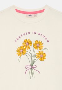 Felpa bianca con un design floreale che presenta margherite gialle, steli verdi e accenti viola, con l'etichetta "PER SEMPRE IN FIORITURA" sopra il graphic.