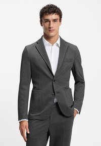 Gray tailored blazer made from textured fabric, featuring a notch lapel, two front pockets, and a single button closure. White shirt underneath.