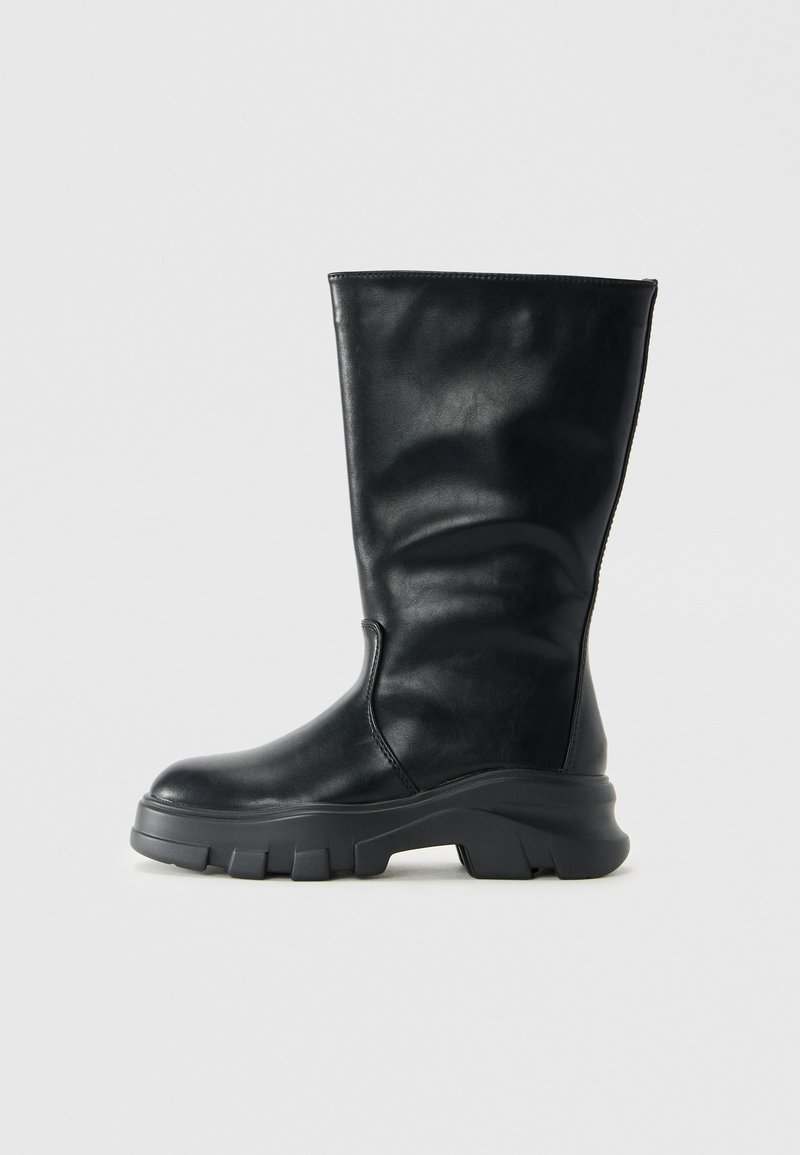 Schwarze Lederstiefel bis zur Mitte der Wade mit dicker, gerippter Sohle und abgerundetem Zehenbereich, seitlich auf einem schlichten, hellen Hintergrund gezeigt.