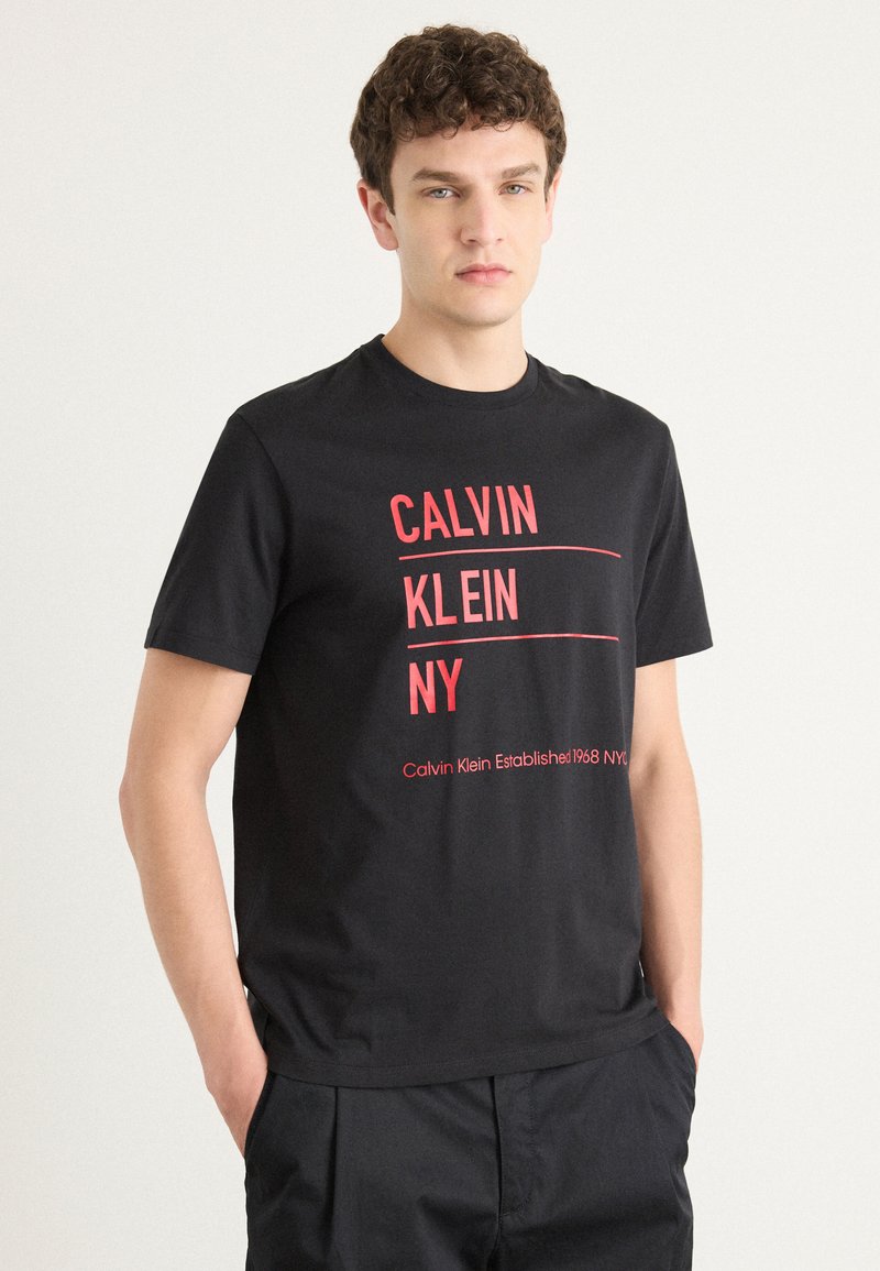 Czarny bawełniany t-shirt z wyraźnym czerwonym napisem: "CALVIN KLEIN NY" oraz "Calvin Klein Established 1968 NYC." Okrągły dekolt, krótkie rękawy.