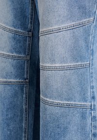 Ljust blå denimbyxor med vertikala sömmar och rak ben-design. Tyget har en slät yta och är nästan utan blekning.