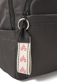 Černý nylonový batoh se zapínáním na zip, stříbrným kroužkem a dekoračním popruhem s červenými a černými vzory. Hladký povrch, kompaktní design.