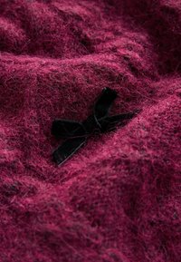 Malvefarbenes strukturiertes Gewebe mit weicher, flauschiger Optik; enthält eine schwarze Samtschleife als Akzent, die in das Material eingearbeitet ist.