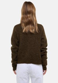 Pull marron doux et court à manches longues, avec une finition texturée. Porté avec un jean blanc, affichant une coupe décontractée.