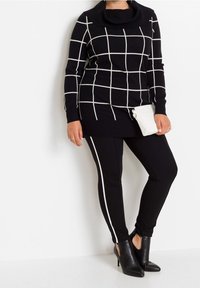 Pull à carreaux noir et blanc avec col bénitier, associé à un pantalon noir doté de bandes blanches sur les côtés et des bottines noires. Pochette blanche.