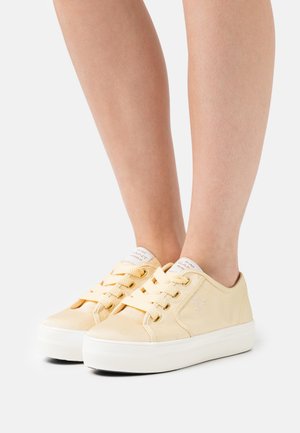 Zapatillas de lona amarillas con suela de goma blanca, con punta redonda, diseño con cordones y marca en la lengüeta. Textura suave.