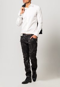 Camicia bianca con bottoni, jeans neri con motivi testurizzati, stivali di pelle nera e una giacca nera gettata sulla spalla.
