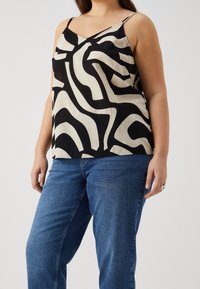 Schwarz-weiß gemustertes Camisole mit dünnen Trägern, versehen mit abstrakten Wellenmustern, kombiniert mit blauen Denim-Jeans. Glatte Textur.