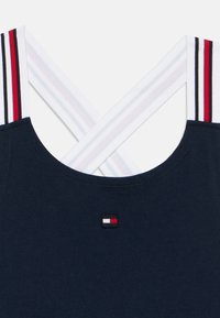 Μπλε μπλουζάκι χωρίς μανίκια με διασταυρούμενους λευκούς ιμάντες με κόκκινες και μαύρες λεπτομέρειες, στρογγυλή λαιμόκοψη και μικρή κεντημένη λεπτομέρεια λογότυπου.