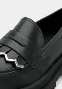 Black leather loafer featuring a flat sole, stitched detailing, and a metallic geometric accent on the upper strap.