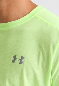Camiseta deportiva verde claro hecha de un tejido texturizado, con un pequeño logo gris en el lado izquierdo del pecho, cuello redondo y mangas cortas.