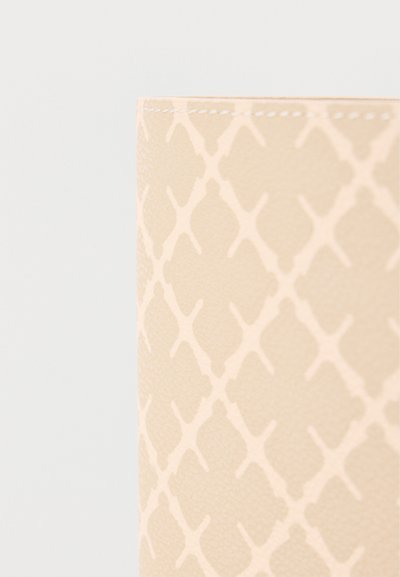 Κοντινή λήψη μπεζ υφάσματος με διακριτικό σχέδιο πλεκτού πλέγματος και εμφανείς λευκές ραφές κατά μήκος του πάνω άκρου.