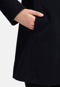 Marineblauwe wollen jas met een gladde textuur, voorzien van een zijzak en strakke lijnen, met een minimalistisch ontwerp.