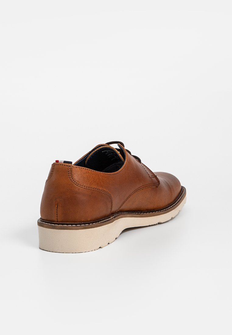 Brązowy skórzany but z zaokrąglonym czubkiem, z beżową podeszwą i akcentami w postaci szwów. Obcas ma gładką fakturę i minimalistyczny design.