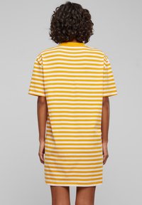 Robe courte à rayures jaunes et blanches avec une coupe décontractée, manches courtes et un ourlet droit. Fabriquée en tissu doux et léger. Vue de dos montrée.