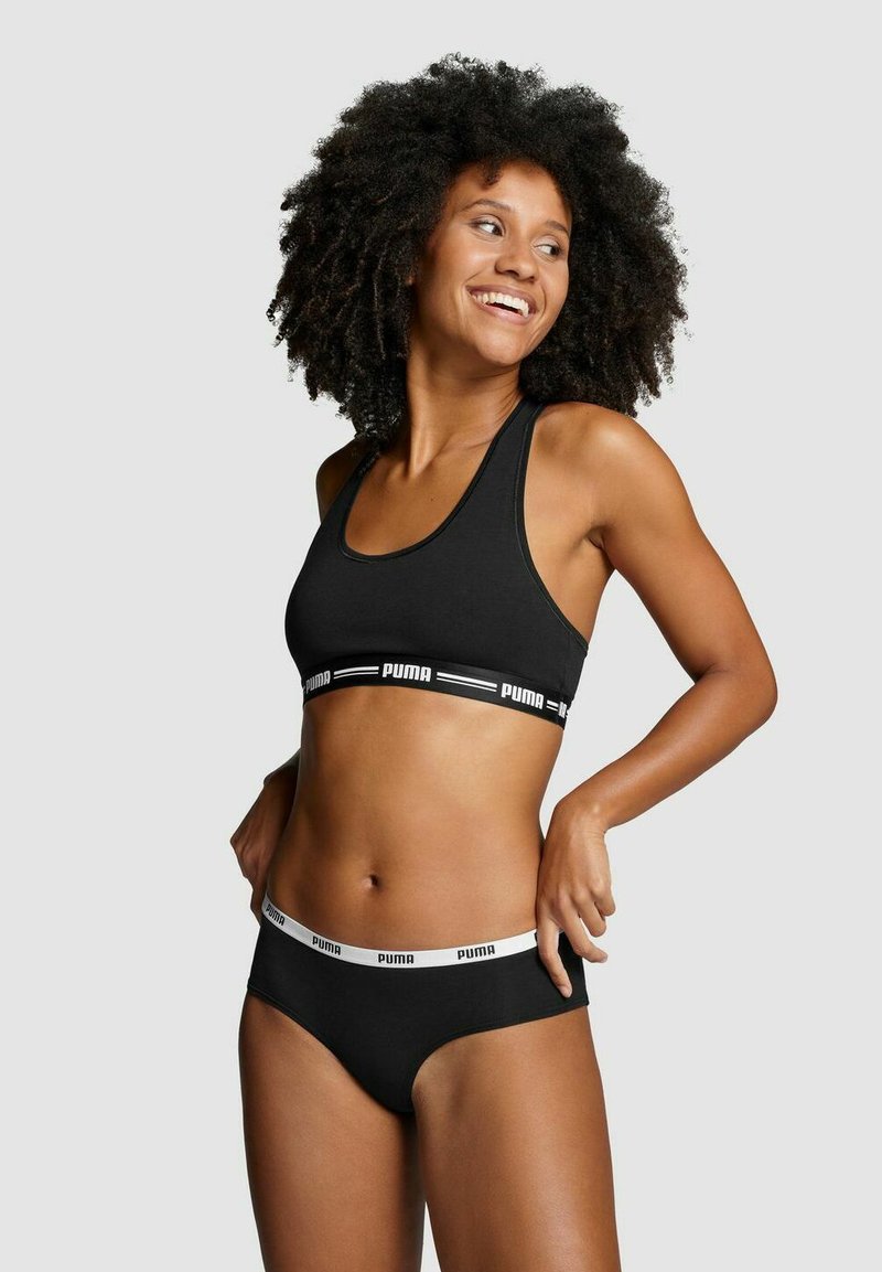 Schwarzer Sport-BH mit PUMA-Logo-Bund und passender schwarzer Unterwäsche. Glattes Material, Racerback-Design und kontrastierende weiße Akzente.