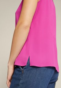 Fuchsia haltertop met een gladde textuur, voorzien van een ronde halslijn en zijsplitten, gecombineerd met blauwe spijkerbroek.