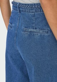 Modre jeans hlače iz denima z spletenim pasom, z dvema zadnjima žepoma in rahlo zbledelim videzom za občutek obrabljenosti.
