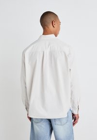 Camicia a maniche lunghe a righe di un beige chiaro con una vestibilità morbida, dotata di colletto e polsini con bottoni, abbinata a jeans in denim azzurro.