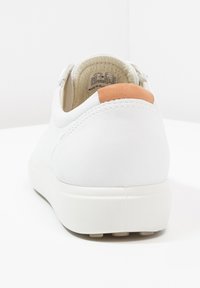 Hvid lavtop-sneaker med tan hælflap, tekstureret gummisål og polstret inderside, vist bagfra på en hvid baggrund.