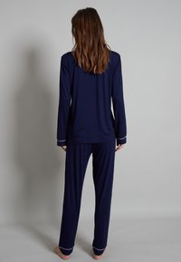 Navy blue pajama set made of soft fabric, featuring long sleeves and pants with white piping along the cuffs and hem.