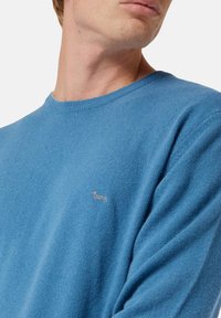 Maglione in lana blu con colletto rotondo, morbido al tatto e un piccolo logo ricamato sul lato sinistro del petto. Maniche lunghe e vestibilità rilassata.