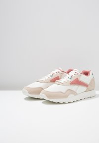 Sneakers leggeri con una tomaia in rete bianca, dettagli in suede beige e un design triangolare rosa sul lato. Suola in gomma per una buona aderenza.