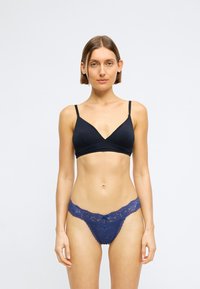 Schwarzer Bralet mit tiefem Ausschnitt und dünnen Trägern, kombiniert mit einem blauen Spitzenslip mit Schleifendetail am Taillenbund.