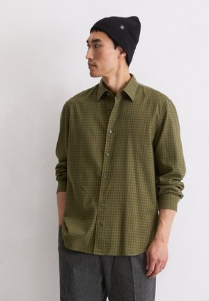 Groen geruite overhemd met een button-down kraag, gemaakt van lichtgewicht stof. Gekoppeld aan een zwarte gebreide beanie en grijze broeken.