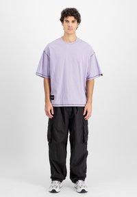 Tricou oversized lavandă cu mâneci scurte, având un etichetă laterală, asortat cu pantaloni cargo negri și adidași argintii.