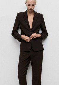 Brown tailored suit with a deep v-neck blazer, single button closure, and straight-leg trousers. Smooth texture and minimalistic design.