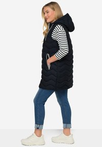 Mjölkblå quiltad väst med huva, med en dragkedja fram och sidofickor. Bärs över en randig långärmad tröja och tillsammans med uppvikta denimjeans.