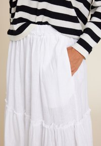 Hvit lin nederdel med samlet lag og elastisk midje, sammen med en svart og hvit stripete genser, som viser komfort og tekstur.