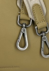 Dos cierres de metal están fijados a una tira de cuero texturizado de un verde oliva claro, con un detalle de costura en un esquema de color gris claro y blanco.