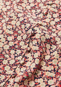 Tissu à motif floral dense en crème, rose et rouge sur fond bleu marine, avec des boutons ronds recouverts de tissu le long d'une couture.