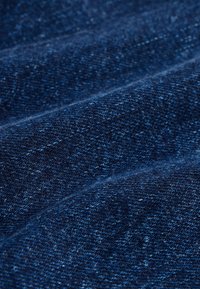 Detailný záber na tmavomodrú rifľovú látku so vzorom tkania a jemnými záhybmi.