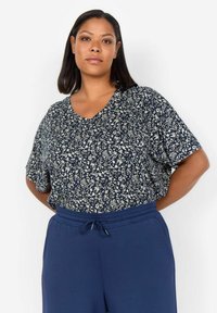 Námornícky blouse s kvetinovým vzorom, hlbokým V-výstrihom a krátkymi rukávmi, v kombinácii s tmavomodrými elastickými nohavicami. Mäkký, ľahký materiál.