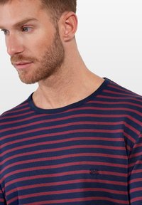 Marineblauwe en bordeaux gestreepte blouse met een ronde halslijn en geborduurd logo op de borst. Zachte, ademende stof met een relaxte pasvorm.
