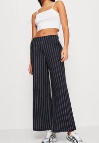 Marinblå vida byxor med vita vertikala ränder, med hög midja och mjukt tyg. Kombinerat med en vit kortärmad tanktopp och joggers.