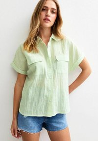 Ljusgrön randig kortärmad skjorta med två framfickor, i kombination med blå denimshorts. Mjuk textur och avslappnad passform.