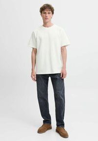 Hvid kortærmet t-shirt med en løs pasform, parret med mørke denim jeans og brune slip-on sko. Simpelt design, minimalistisk stil.