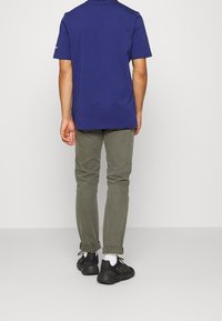 Námořnické tričko s krátkým rukávem, olivové kalhoty s ohrnutými manžetami, černé tenisky a bílé ponožky. Jednoduchý design, bavlněná látka a volný střih.