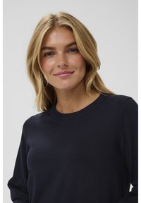 Pull en tricot bleu marine avec un col rond côtelé, des manches longues et une texture lisse, mettant en avant la simplicité du design.