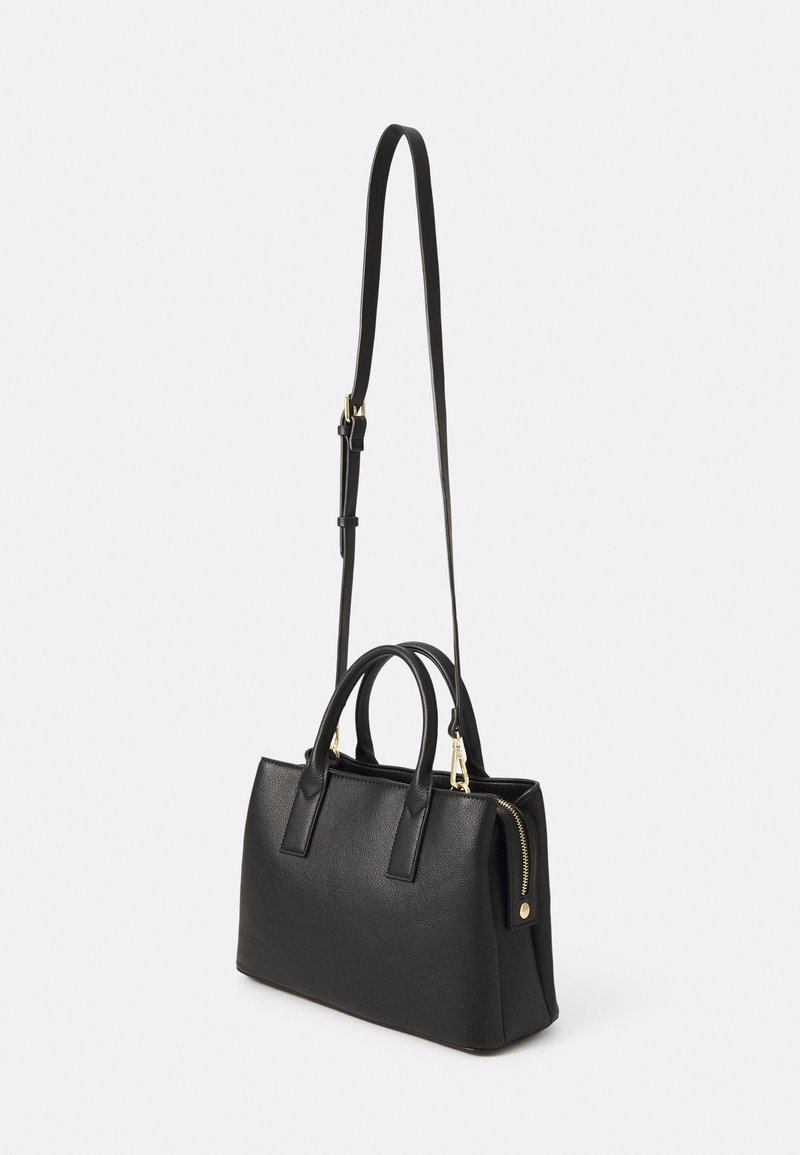 Sac à main en cuir noir avec deux poignées, une longue bandoulière réglable et une fermeture éclair dorée sur le côté sur fond blanc.